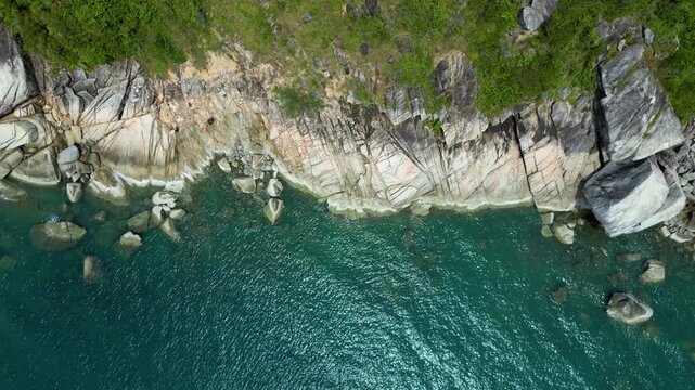 Cinematic drone footage of a rocky beach captured from a 90-degree top-down angle in Thailand. The video highlights natural rock formations along the coastline, ocean waves, and textured shoreline pat