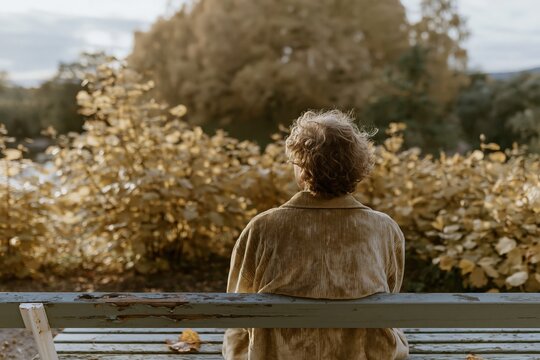 Young man sitting alone on a weathered park bench gazing at warm honey gold foliage for mindfulness and mental health imagery