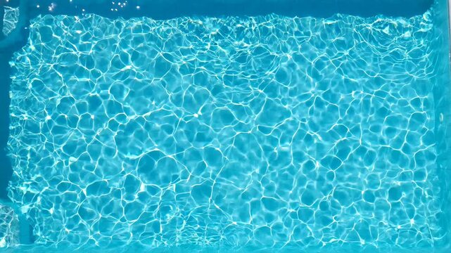 Clear turquoise swimming pool water with sun glare, ripples and caustic reflections moving in slow motion, creating a relaxing and abstract summer vacation background