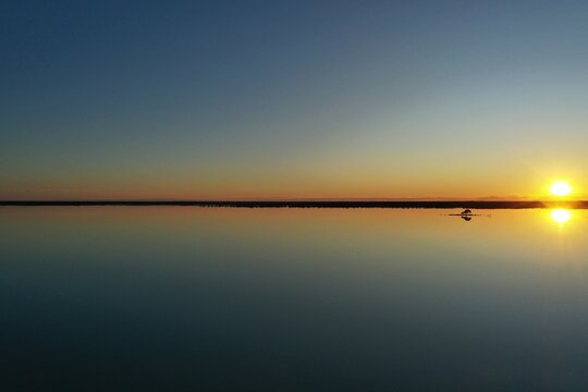 Aerial view of Lake Machattie at sunset with calm water reflecting the golden light in Bedourie, Queensland, Australia.