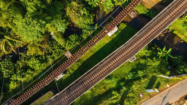 Aerial view of the Serongan railway bridge crossing lush green vegetation and a river in Kecamatan Cilongok, Jawa Tengah, Indonesia.