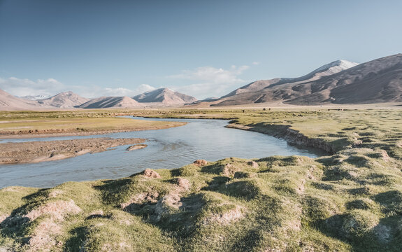 Clear-water rivers and lakes in a mountain valley, pastures and green grassy fields set against mountain ranges and snow-capped, glacier-clad peaks&mdash;a scenic landscape background