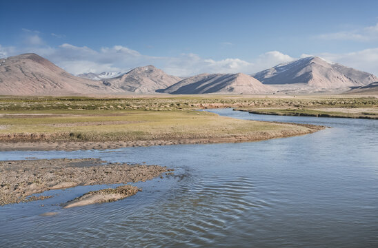 Clear-water rivers and lakes in a mountain valley, pastures and green grassy fields set against mountain ranges and snow-capped, glacier-clad peaks&mdash;a scenic landscape background