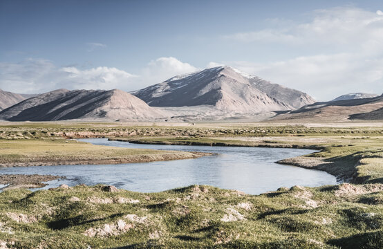Clear-water rivers and lakes in a mountain valley, pastures and green grassy fields set against mountain ranges and snow-capped, glacier-clad peaks&mdash;a scenic landscape background