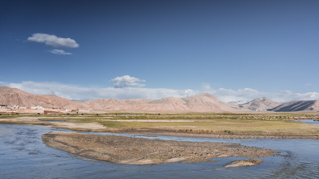 Clear-water rivers and lakes in a mountain valley, pastures and green grassy fields set against mountain ranges and snow-capped, glacier-clad peaks&mdash;a scenic landscape background