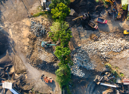 Aerial view of the Babakan quarry site with excavators, dump trucks, and piles of rocks, with a line of trees separating the work areas in Karanglewas, Central Java, Indonesia.
