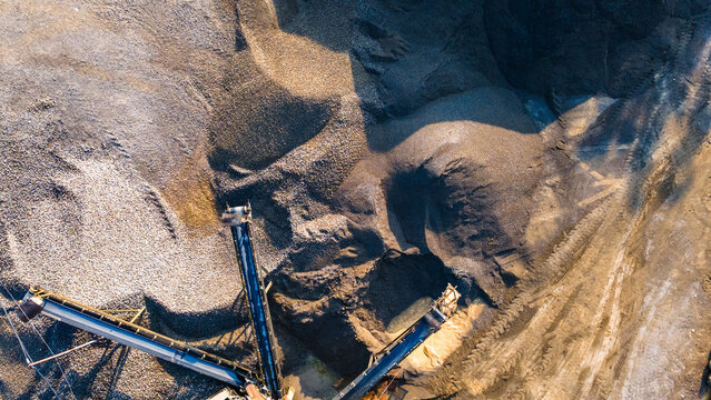 Aerial view of a mining site with conveyor belts transporting gravel and sand, showing large piles of aggregate in Karanglewas, Central Java, Indonesia.