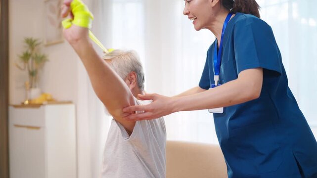 Professional caregiver guiding elderly man through resistance band exercise at home improving upper body strength mobility rehabilitation and healthy aging with personalized senior physical therapy