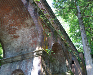 Naklejka premium Historic Red Brick Aqueduct Suirokaku Surrounded by Lush Green Trees in Kyoto
