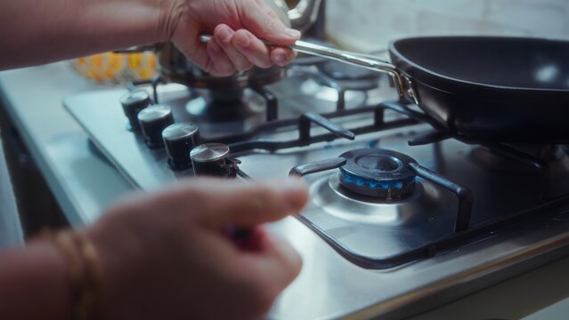 Person adjusting gas flame on a modern stainless steel stovetop while holding a black frying pan handle