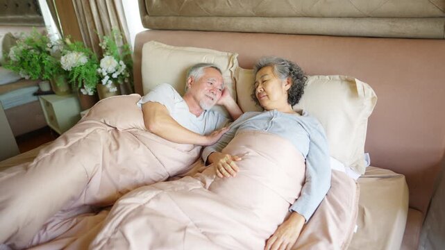 Happy Asian senior couple sleeping together in bed at home, elderly husband and wife embracing during peaceful rest, loving relationship and comfortable retirement lifestyle with aging gracefully