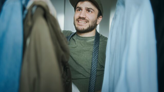 Young man feeling indecisive and overwhelmed while choosing clothes from a crowded wardrobe in a casual setting