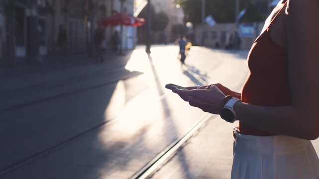 Close-up: a young woman holding a smartphone. She is using her mobile phone outdoors against an urban backdrop. urban lifestyle.