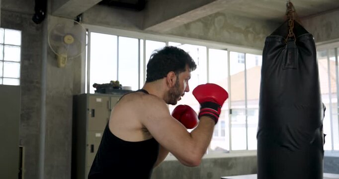 Adult Caucasian man works heavy bag from side angle in modern gym, shifting guard and delivering punches. Male athlete trains boxing technique, endurance, coordination, strength, active routine.