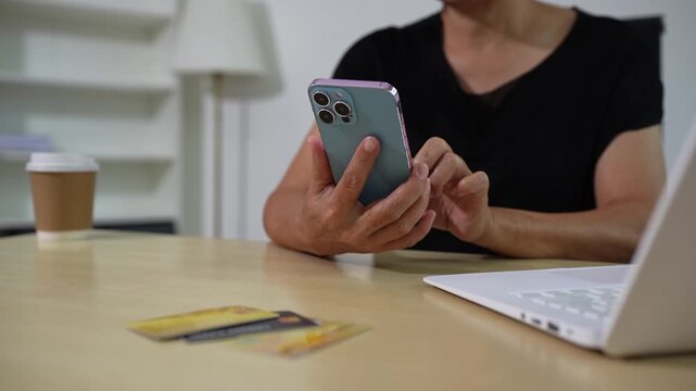 Mature women use smartphone for laptop payments, online shopping, omni channels, sitting at desk.