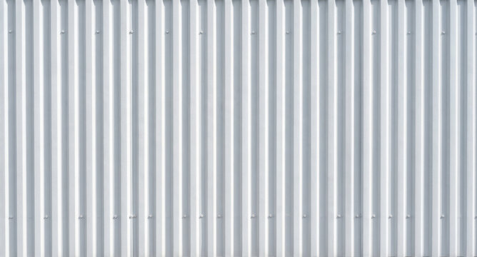 A long, vertical corrugated metal wall is presented against a black background. The metal has a smooth, reflective surface with repeating, parallel ridges.