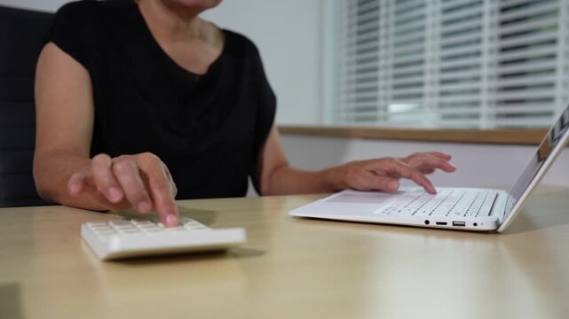 woman working on laptop and accounting financial report, accountant using calculator to calculate tax refund at office