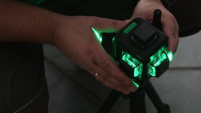 Close-up of worker setting up a green laser level for accurate alignment and measurement during construction, installation or industrial engineering work.
