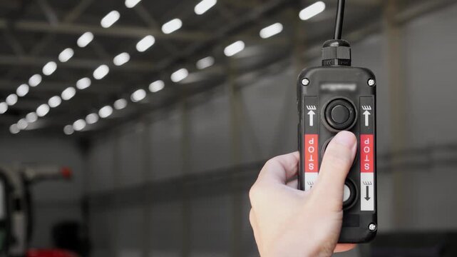 Close-up of worker operating a wired industrial crane controller inside a modern manufacturing facility. Industrial automation, material handling and factory operations.