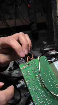 Technician hands inserting connector wires into a green printed circuit board