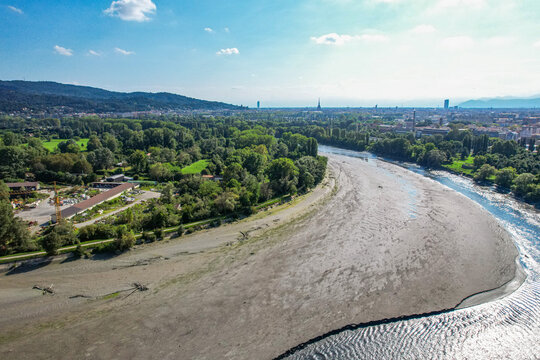 Aerial view of the dry riverbed at the confluence of the Stura and Po rivers with surrounding lush vegetation and the city skyline in Torino, Piemonte, Italy.