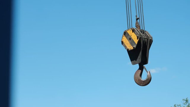 Close-up of a heavy-duty mobile crane hook suspended against blue sky before lifting industrial cargo. Construction, rigging and heavy equipment concept.