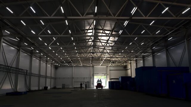 Wide view of a modern industrial warehouse with LED lighting, forklift, storage space and manufacturing infrastructure. Logistics, production and distribution facility.