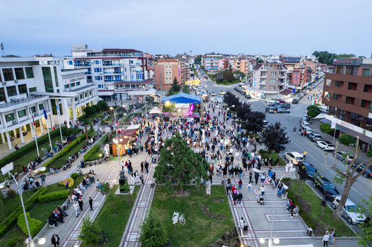 Primorsko, Bulgaria - 24 May 2025: Aerial view of a lively town square with a stage, crowds of people, surrounding modern buildings, and green park areas under a clear evening sky.