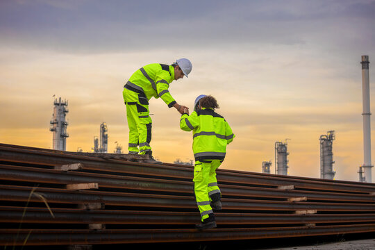 Engineers helping each other climb on construction materials at an industrial site, Professional team in high-visibility gear working together at a factory project
