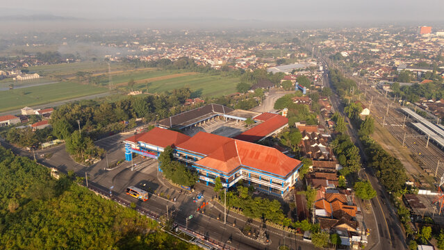 Indonesia - 19 June 2026: Aerial view of a large terminal building with a red roof, adjacent to a railway station and surrounded by urban infrastructure and green fields.