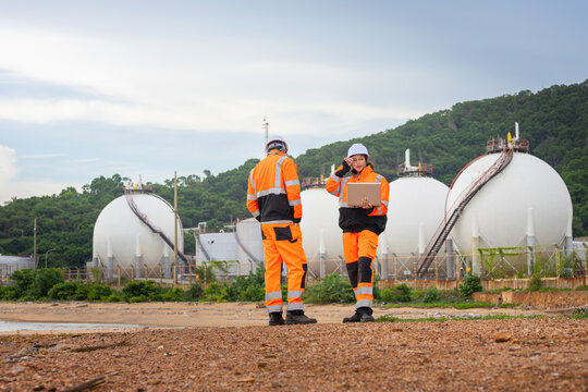 Team of technicals in safety uniform discussing maintenance plan at fuel storage facility, Industrial engineers team with laptop and radio to monitor gas storage tank system