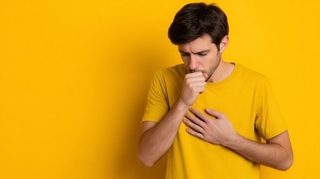 Man coughs while holding his chest against a bright yellow background during the autumn virus season