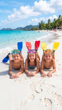 Three cute Caucasian siblings children resting on white sand of a tropical beach, wearing snorkeling masks and colorful flippers, smiling during a sunny summer vacation