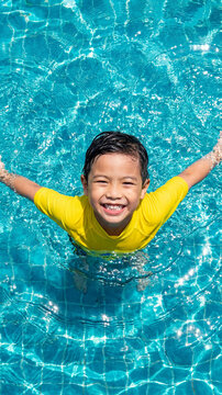 Asian boy with a big smile swims in a blue pool on a sunny day, top view. Fun summer vacation and travel concept