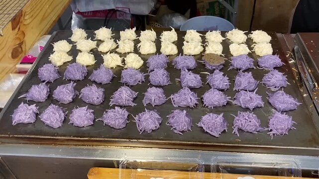Authentic, Famous Khanom Babin, a Thai Traditional Coconut Milk Pancake Macaroon Fritter Dessert. Cooking on Fresh Hot Skillet at a Open Street Food Night Market in Bangkok Thailand