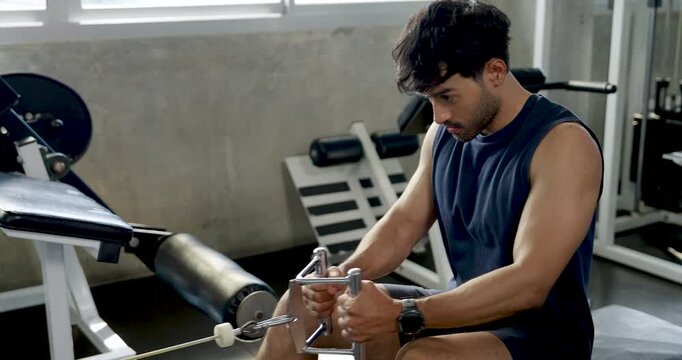Young Asian man continues seated cable row workout in modern gym, pulling handle toward chest with steady form, solo upper body strength training, arm muscle routine, wellness, healthy lifestyle.