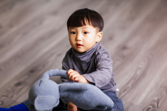 A cute Asian boy wearing a gray sweater plays indoors.