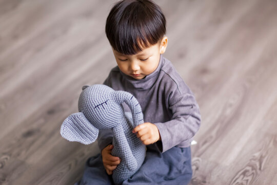 A cute Asian boy wearing a gray sweater plays indoors.