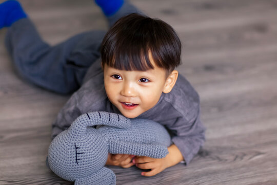 A cute Asian boy wearing a gray sweater plays indoors.