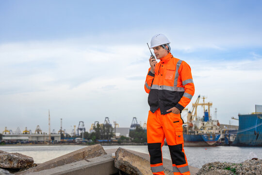 Logistics engineer using walkie-talkie to coordinate operations at shipping port, Worker communicating with radio at container terminal, Marine logistics specialist managing cargo transport activities