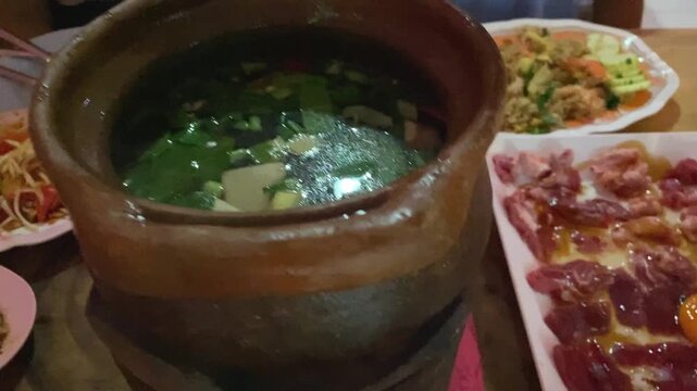 Hand Opens Lid, Jim Jum Thai Clay Hotpot Isaan Style Traditional Soup with Raw Pork Beef Meat & Herbs Vegetables. Asian Street Food Restaurant in Bangkok Thailand.