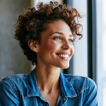 Woman smiles while looking out a window during daylight in a cozy indoor space