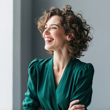 Smiling woman stands by a window in a bright room during daytime wearing a green dress