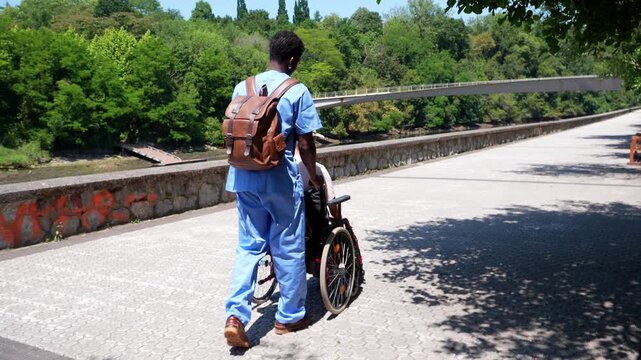 Young caregiver assisting an elderly person in a wheelchair during a sunny day walk in the park. Supportive healthcare professional providing compassionate assistance and companionship outdoors