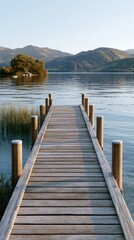 Fototapeta premium Wooden dock extending over calm lake water with mountains in the background and lush greenery along the shoreline under clear blue sky