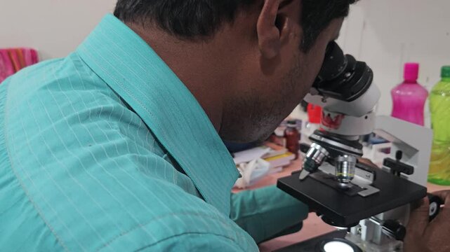 Scientist examining laboratory sample using optical microscope in modern research laboratory. Researcher focusing on microscopic analysis, scientific observation, laboratory diagnostics