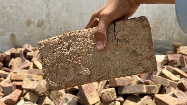 Hand holding a single stone brick over a pile of rubble