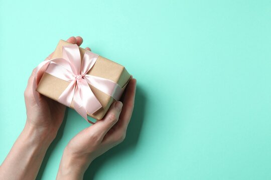Woman's hands holding giftbox with pink satin ribbon bow on pastel background, space for text. Top view