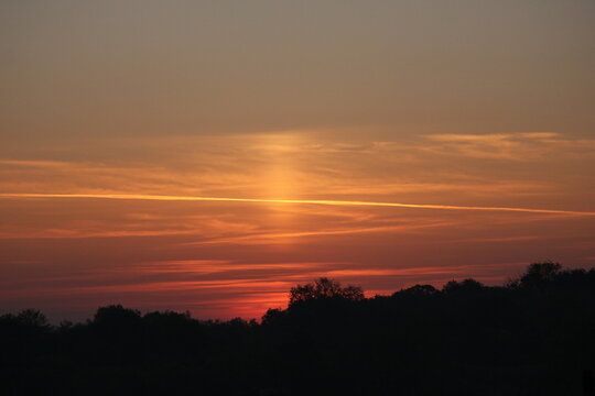 An ice pillar shortly before sunrise, above a tree line, clouds and contrails