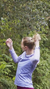 Vertical video: Tying hair runner in lilac top and pink tights fixing tie in woods prepping to run